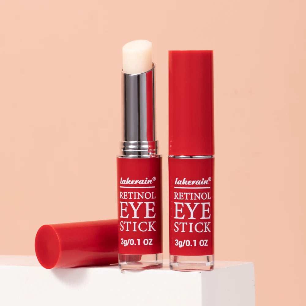 Professional studio shot of two Lakerain Retinol Eye Sticks on a white pedestal against a peach background, showing the open balm and closed applicator.